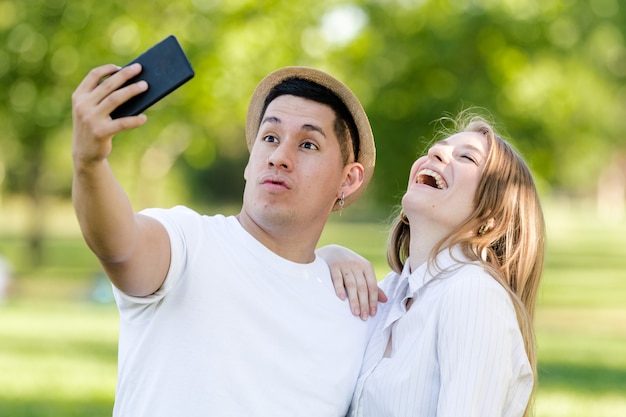 Junges Paar, das ein Selfie auf ihrem Handy im Park nimmt. Lateinischer Mann und kaukasische Frau