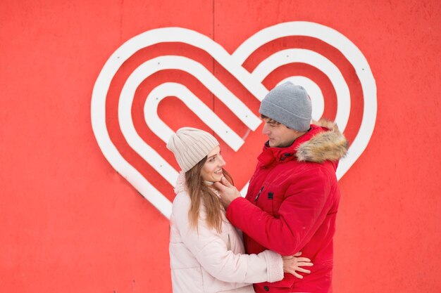 Junges Paar, das einander nahe großes Herz an der Wand ansieht. Valentinstag