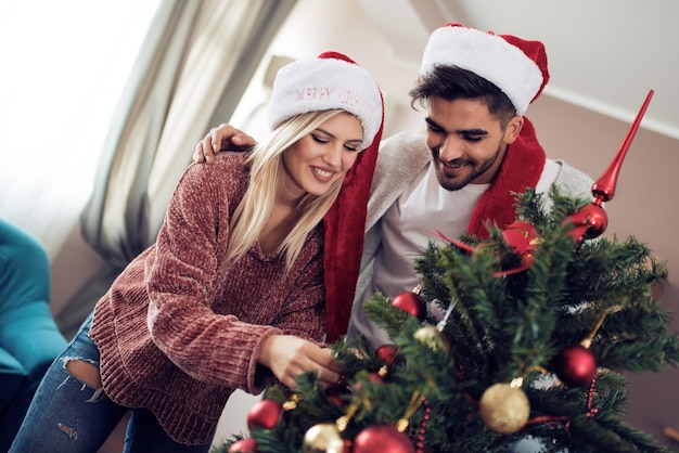 Junges Paar, das einen Weihnachtsbaum schmückt