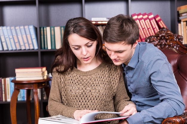 Junges Paar, das ernsthaft ein Buch liest, während es auf einem so geschlossenen Stuhl in der Bibliothek sitzt.