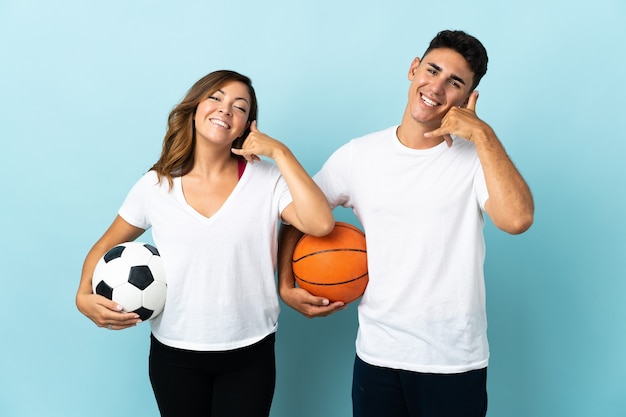 Junges Paar, das Fußball und Basketball auf blau macht Telefon Geste macht. Rufen Sie mich zurück Zeichen