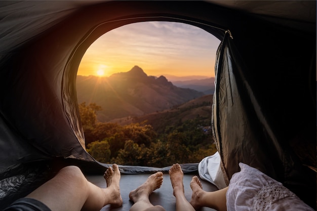 Junges Paar, das im Campingzelt liegt und Sonnenuntergang über dem Berg betrachtet