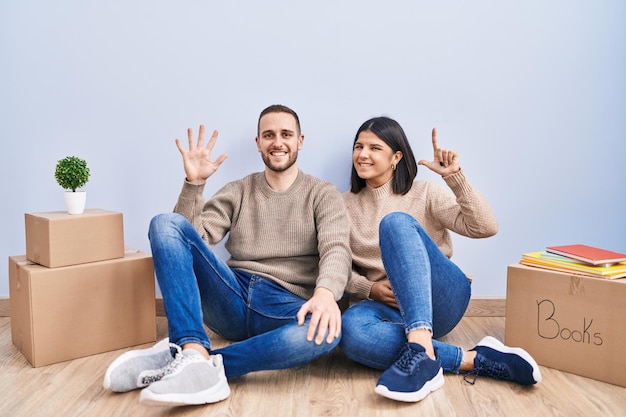 Junges Paar, das in ein neues Zuhause umzieht, zeigt und zeigt mit den Fingern Nummer sieben nach oben, während es selbstbewusst und glücklich lächelt
