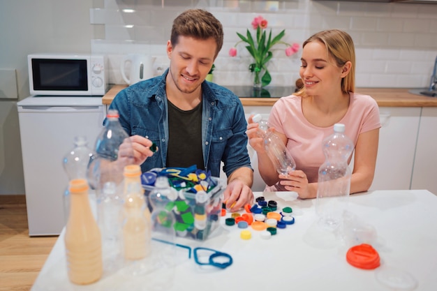 Junges Paar, das leere Plastikflaschen und -deckel wiederverwertet