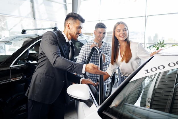 Junges Paar, das sich im Autohaus ein Auto auswählt, wobei der Manager hilft