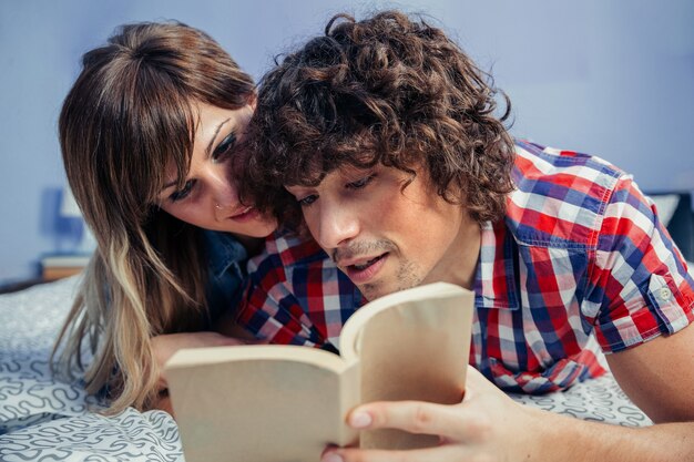 Junges Paar, das zusammen ein Buch liest, das auf dem Bett liegt
