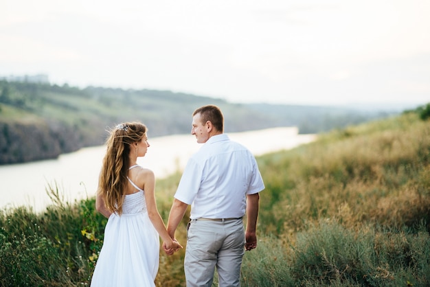 Junges Paar, ein Mädchen und ein Mann, gehen auf dem Feld vor dem Hintergrund des Flusses