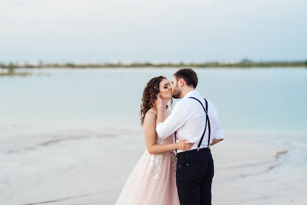 Junges Paar, ein Mann in schwarzen Reithosen und ein Mädchen in einem rosa Kleid, gehen durch den weißen Sand der Wüste