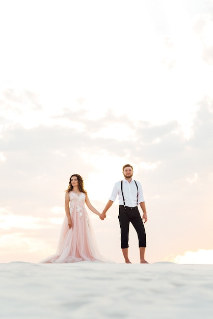Junges Paar, ein Mann in schwarzen Reithosen und ein Mädchen in einem rosa Kleid, gehen durch den weißen Sand der Wüste