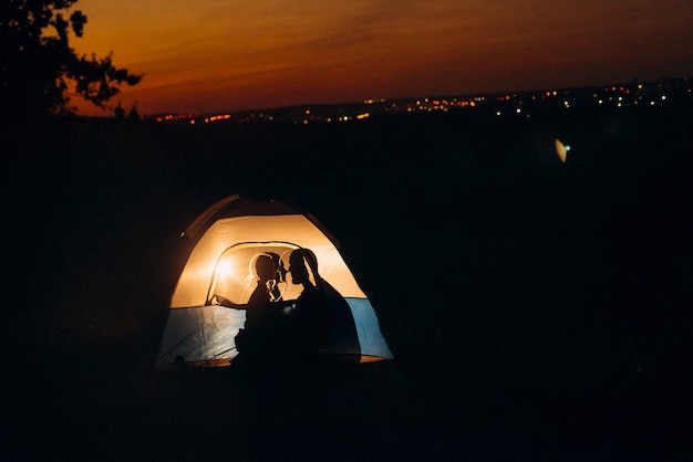 Junges Paar, ein Mann und ein Mädchen in hellen Strickmützen, hielten auf einem Campingplatz in der Nähe des Feuers an