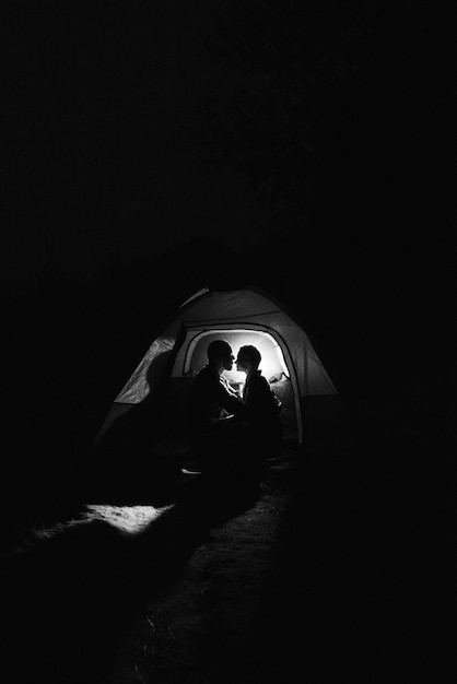 Junges Paar, ein Mann und ein Mädchen in hellen Strickmützen, hielten auf einem Campingplatz in der Nähe des Feuers an