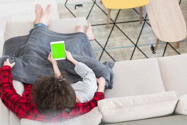 Junges Paar entspannt sich zu Hause mit Tablet-Computern und liest im Wohnzimmer auf der Sofacouch.