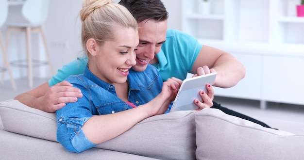 Junges Paar Entspannung im luxuriösen Haus mit Tablet-Computer lesen im Wohnzimmer auf der Sofa-Couch.