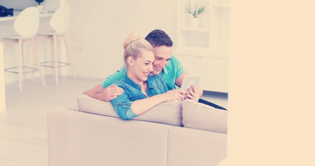 Junges Paar Entspannung im luxuriösen Haus mit Tablet-Computer lesen im Wohnzimmer auf der Sofa-Couch.