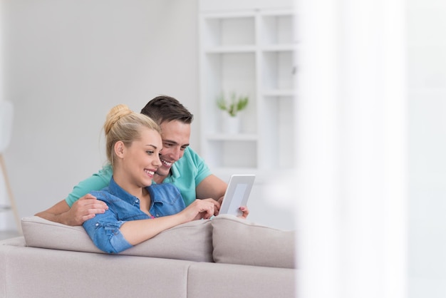Junges Paar Entspannung im luxuriösen Haus mit Tablet-Computer lesen im Wohnzimmer auf der Sofa-Couch.