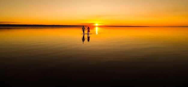 Junges Paar geht am Sommerstrand im Wasser weg. Sonnenuntergang über dem Meer. Zwei Silhouetten gegen die Sonne. Gerade verheiratetes Paar in der romantischen Liebesgeschichte. Mann und Frau im Urlaub Flitterwochen.