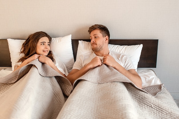 Junges Paar im Bett. Angst vor Sex, schüchterne Frau und Mann, die sich vor Intimität unter der Decke verstecken