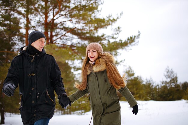 Junges Paar in der Liebe, die im verschneiten Winterwald läuft und Hände hält