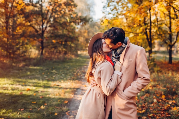 Junges Paar in der Liebe geht im Herbstwald zwischen bunten Bäumen. Stilvolle Leute, die bei Sonnenuntergang umarmen und küssen