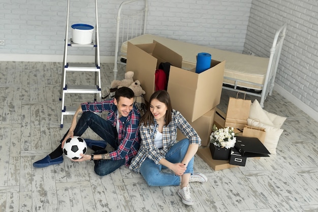 Junges Paar in einem neuen Zuhause, das sich auf dem Hintergrund großer Kisten entspannt. Konzept Housewarming, begann zusammen zu leben.