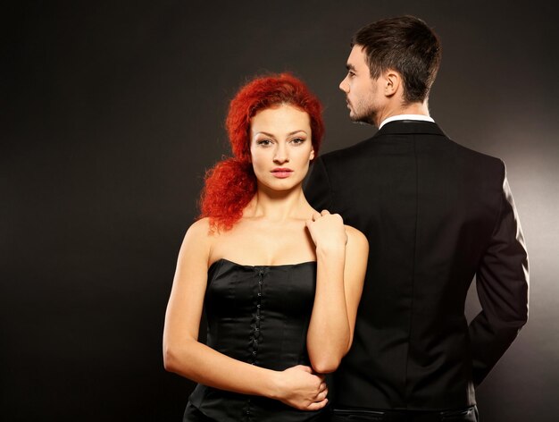 Junges Paar in Kleid und Anzug stehen zusammen auf schwarzem Hintergrund