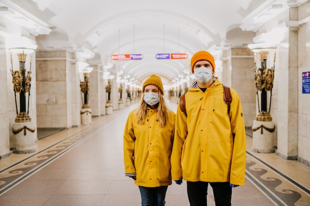 Junges paar in medizinischen schutzmasken, die gelbe windjacken an der leeren u-bahnstation tragen und an die virusabdeckung-19 denken. coronavirus-pandemiekonzept.