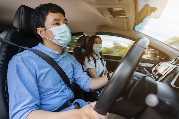 Junges Paar in medizinischer Maske beim Autofahren. zum Schutz der Covid-19 (Coronavirus)-Pandemie