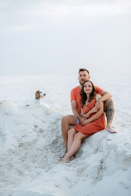 Junges Paar in orangefarbener Kleidung mit Hund im weißen Wüstensand