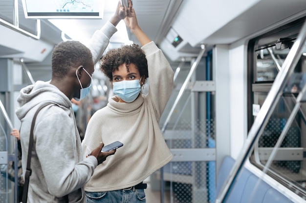 Junges Paar in Schutzmasken, das in einem U-Bahn-Wagen steht