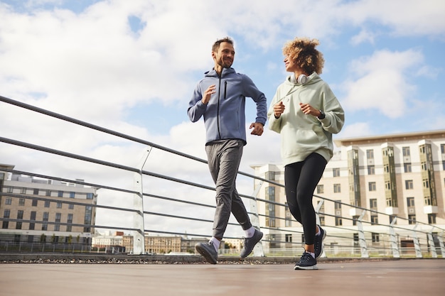 Junges Paar in Sportkleidung, die zusammen auf der Stadtstraße joggt