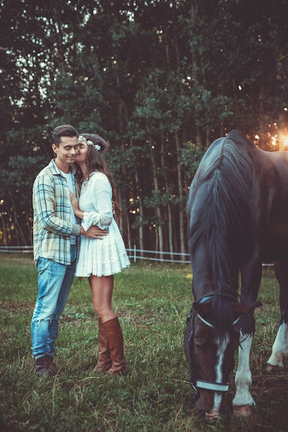 Junges Paar in Umarmung auf der Wiese mit einem Pferd