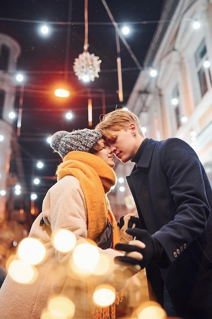 Junges Paar in warmer Kleidung küssen auf weihnachtlich dekorierter Straße.
