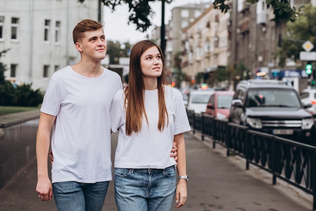 Junges Paar in weißen T-Shirts und Jeans geht durch die Straßen der Stadt und hält Hände.