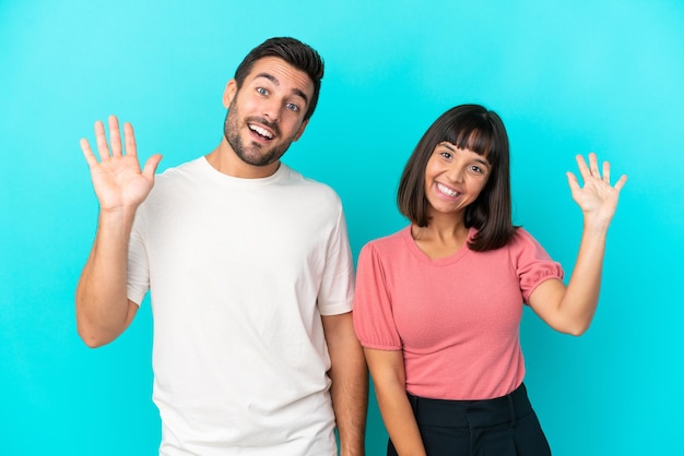Junges Paar isoliert auf blauem Hintergrund, das mit der Hand mit glücklichem Ausdruck grüßt