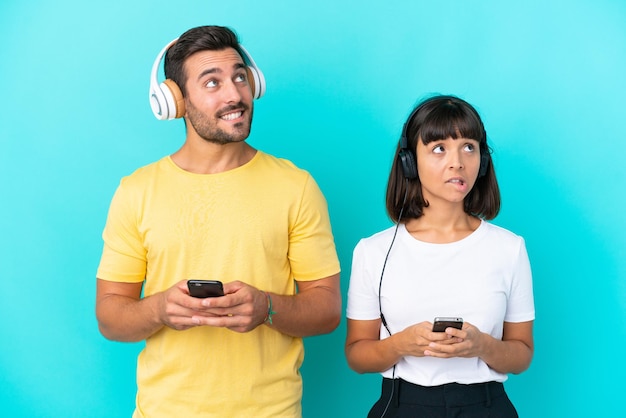 Junges Paar isoliert auf blauem Hintergrund Musik hören mit einem Handy und Denken