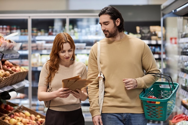 Junges Paar kauft im Supermarkt Lebensmittel ein und hält Papiertüten in der Hand
