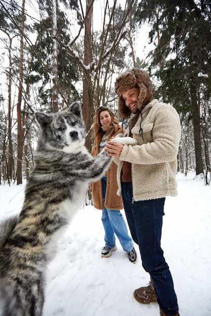 Junges Paar lächelt und hat Spaß im Winterpark mit ihrem Husky-Hund