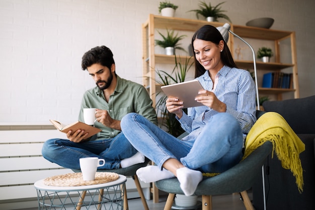 Junges Paar liest zusammen Buch und E-Book, sitzt auf der Couch