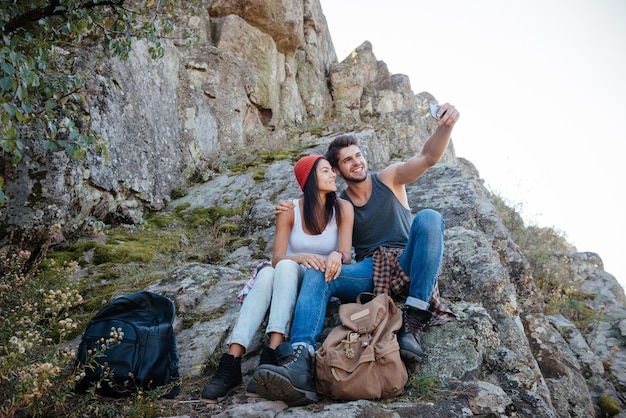 Junges Paar macht Selfie und sitzt auf Felsen. Bild in voller Länge