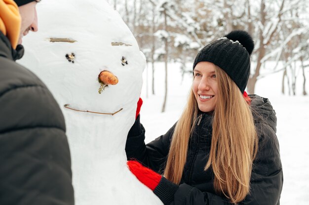 Junges Paar machte einen Schneemann in einem verschneiten Park