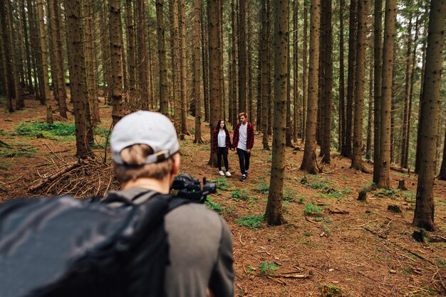 Foto junges paar, mann und frau in roten hemden, die händchen haltend durch den wald gehen