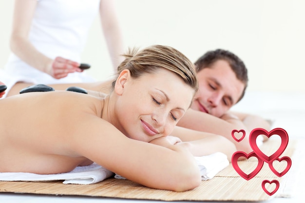 Junges Paar mit einer Massage mit heißem Stein gegen rosa Herzen