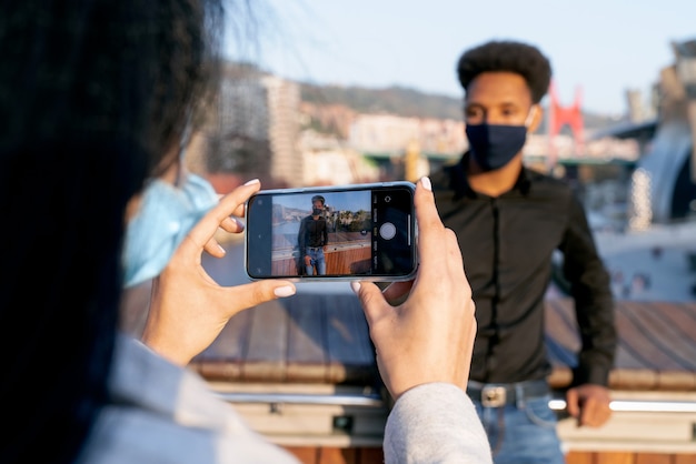Junges Paar mit jungen Afro-Stil Haaren auf der Straße, die ein Foto mit ihrem Handy machen, weil sie Bilbao mit einer Gesichtsmaske wegen der Coronavirus-Pandemie covid-19 von 2020 besuchen