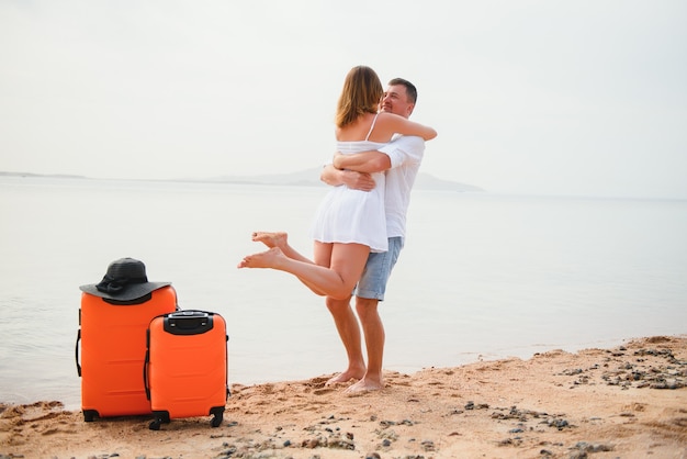 Junges Paar mit Koffer am Strand im Sommertag.
