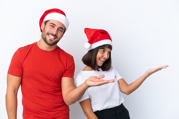 Junges Paar mit Weihnachtsmütze isoliert auf weißem Hintergrund zeigt nach hinten und präsentiert ein Produkt