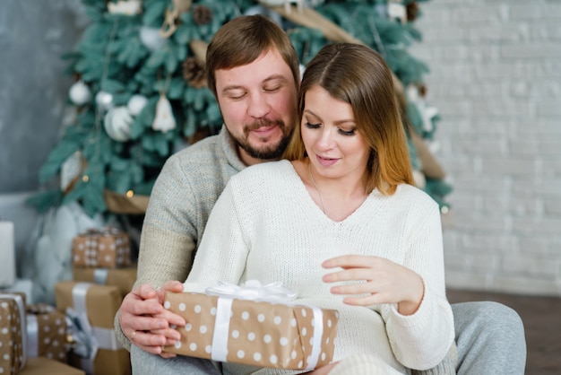 Junges Paar nahe Weihnachtsbaum. Frau mit Ehemann. Mann, der Mädchen umarmt. Neujahrsgeschenkbox.