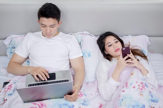 Junges Paar nutzt digitale Geräte vor dem Schlafengehen