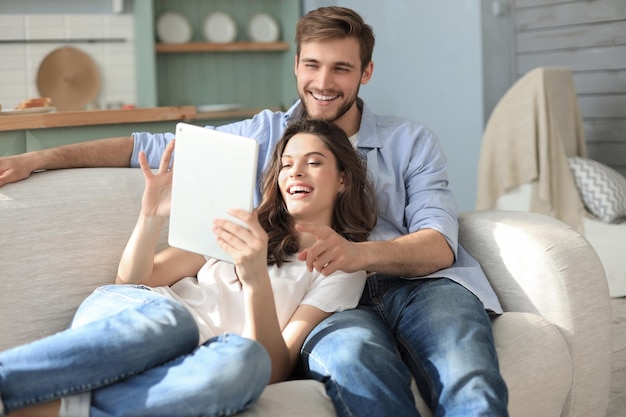 Junges Paar sieht sich Medieninhalte online auf einem Tablet an, das auf einem Sofa im Wohnzimmer sitzt.