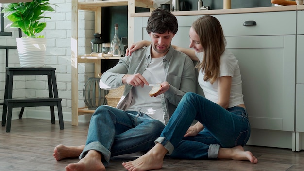 Junges Paar sitzt auf dem Küchenboden und verteilt Butter auf Brot