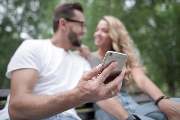 Foto junges paar sitzt auf einer bank und benutzt smartphone